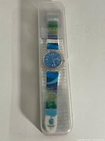 Full view of Swatch SUDK103F watch in clear plastic box