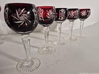 Five ruby red cut crystal wine goblets lined up showing bowl, stem and foot details