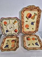 Four ceramic serving pieces displayed upright showing fruit motif and shapes