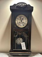 Front view of wooden wall clock showing dial and pendulum