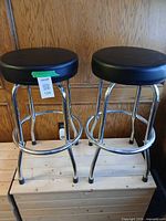 Two chrome bar stools with black leather seats on wooden surface