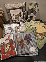 Group shot of all chicken motif items including placemats, pillow, pillow covers, tablecloth, candles, snuffer, notepad and pen