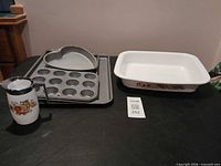 All items arranged on table: CorningWare dish, pour pitcher, four grey metal bakeware pieces