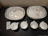 Two oval casseroles with lids and four mugs overview