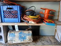 Shelf with boxed cable chains, multiple coiled extension cords, cord reel, cord winders, blue crate