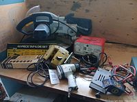 All items displayed together including mitre saw, tap & die set, jigsaw, impact wrench, battery charger, cables and converter