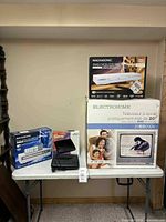 Overall shot showing Electrohome TV/DVD combo box, Magnasonic DVD player box, boxed VHS rewinder and loose VHS rewinder on table