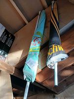 Rolled Coca-Cola and Schweppes branded patio umbrellas on shelf