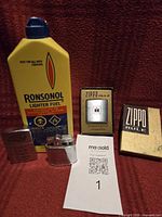 Group shot showing Ronsonol lighter fuel, Zippo Rule tape measure in box, two lighters, auction tag