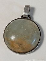 Front view of round sterling silver pendant with pale grey-white cabochon and rust band