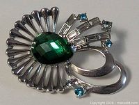 Front view of silver-tone fan brooch with green glass center and blue rhinestones