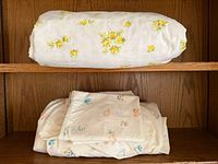 Both quilts folded on shelf: yellow floral rolled on top, pastel floral folded below