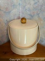 Front angled view of cream George Briard ice bucket showing handle and lid with wood knob