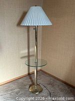 Full view of brass floor lamp with glass shelf and pleated shade