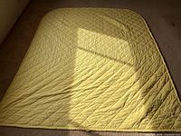 Full view of yellow quilt laid flat showing diamond quilting and rounded top corners