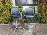Front view of both matching black vinyl swivel bar stools showing upholstery, footrests and bases