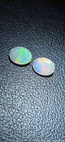 Two oval faceted opals showing multicolor play-of-color on black surface