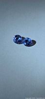 Pair of round violet-blue tanzanite stones on neutral background