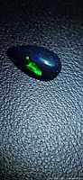 Pear-shaped black opal cabochon showing green and blue play-of-color on textured background