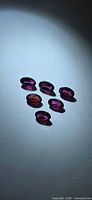 Six oval pink-purple rhodolite garnets on grey background