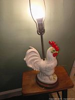 Full view lit, showing ceramic rooster on wooden base with bulb lit