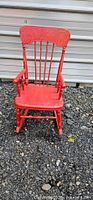 Front view of red distressed wooden kids rocking chair showing carved crest, spindle back and turned legs