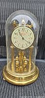 Full view of Ridgeway anniversary clock under glass dome showing dial, base and pendulum