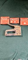 Arrow T50 staple gun and three boxes of T50 staples on green surface