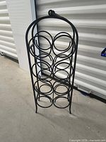 Front view of black wrought iron wine rack showing eight circular holders and arched top