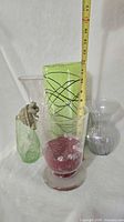 group of five glass vases and turtle figurine with tape measure indicating height of lime green vase