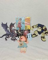 Group shot showing Brat doll, dragon figure, monster figure, hopscotch record sleeve and pink ball