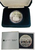 1984 coin in open green velvet box and 1985 coin in grey presentation case