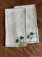 Two folded linen napkins showing corner ivy embroidery and stitched border