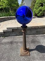 Full view of cast iron post with blue gazing ball on driveway