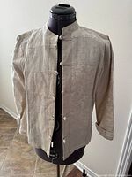 Front view of beige cotton-linen jacket on mannequin showing knot button closure and mandarin collar