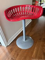 Full view of stool showing red tractor seat and grey pedestal base