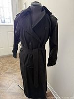 Front view of black Burberry trench coat on mannequin, belt tied, double-breasted layout visible