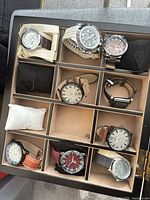 Open display case showing eight wristwatches in separate compartments