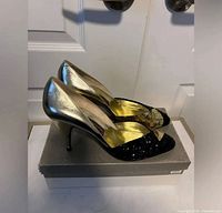 Side view of both pumps on shoe box showing gold leather uppers, black sequin toes, stiletto heels