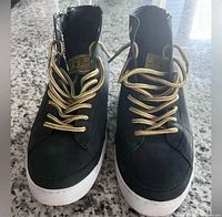 Front view pair of black high-top sneakers with gold laces and white soles
