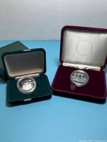 Both commemorative coins open in their velvet cases showing obverse designs