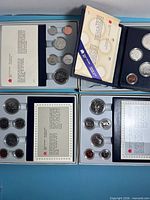 Overview of four open specimen sets showing certificates and coins