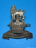 Front view of brass Canadian Provost Corps cap badge on blue background
