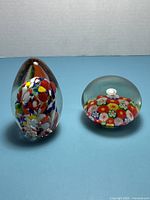 Egg-shaped and round dome millefiori glass paperweights side by side