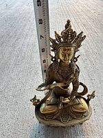 Front view of brass Buddha statue with ruler showing height