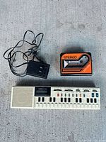 Keyboard, power adapter and Walkman cassette player shown together on floor