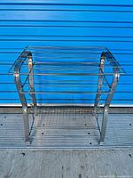 Front view of chrome metal vinyl rack showing top slats and lower mesh shelf