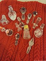 Group of 13 assorted crystal and glass bottle stoppers on red knit background