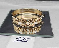 Overall view of goldtone hinged bangle on mirror showing ornate front