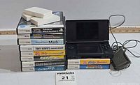 Stack of DS game cases, loose cartridges on top, DS Lite console and charger beside stack